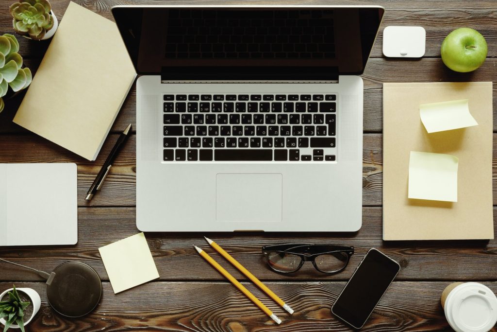 Office desk with laptop computer, supplies and green apple, top view